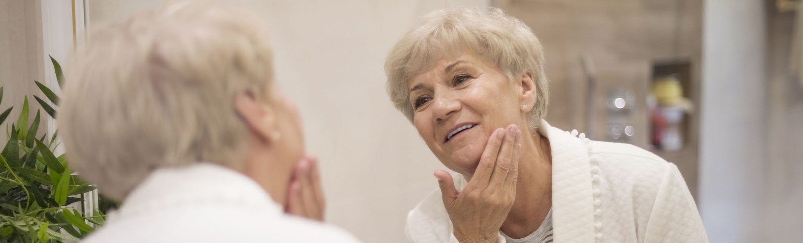 Ältere Frau betrachtet das Ergebnis ihrer Eigenfettunterspritzung im Gesicht in den Moser Kliniken im Spiegel