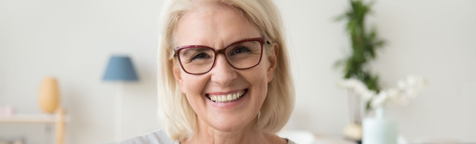 Blonde Frau mit Brille kann nach Unterspritzung der Nasolabialfalte wieder freudig lächeln